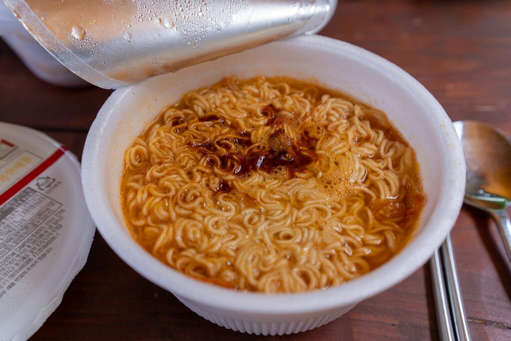 A close-up of a steaming bowl of instant noodles with a focus on the salt-heavy seasoning powder