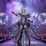 Lady Gaga performing on stage during her Mayhem Ball Tour, wearing a dramatic avant-garde costume.